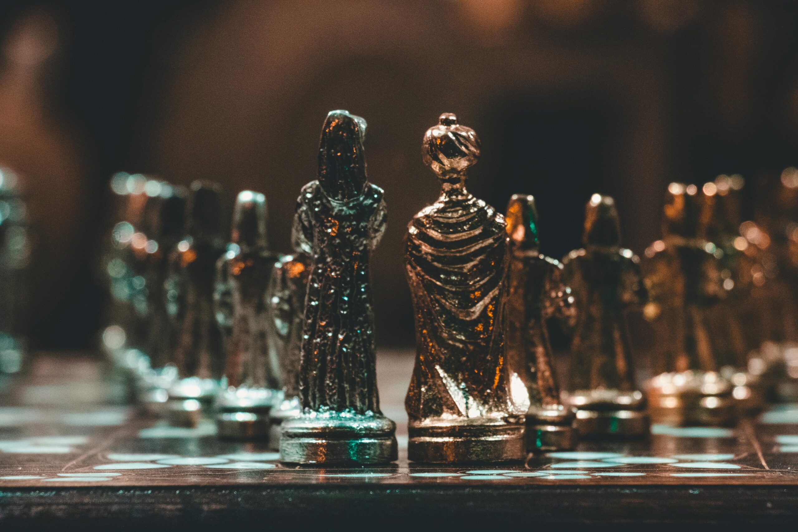 Close-up of gold chess pieces on a chessboard in a dimly lit room.