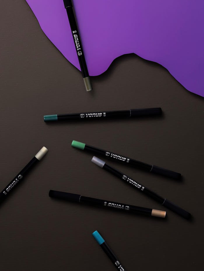 Stylish arrangement of vibrant eyeliners on a rich dark backdrop with purple accents, perfect for beauty and fashion editorial.