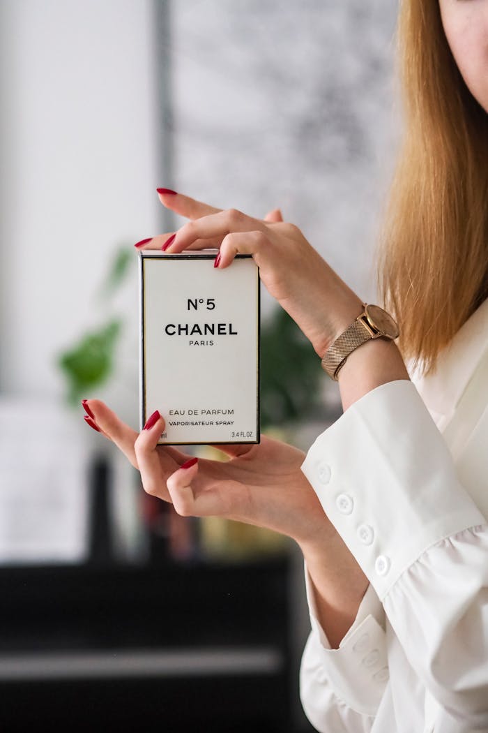 Close-up of Chanel No.5 held by a woman with red nails and a gold watch.