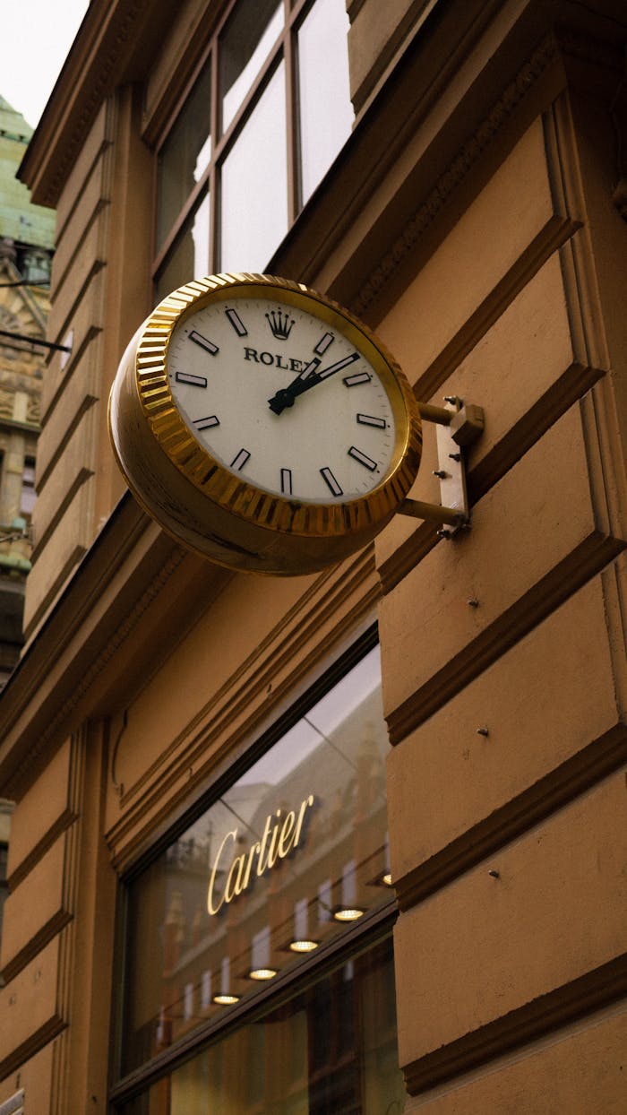 A vintage Rolex wall clock mounted on a historic building facade above a Cartier store, captured outdoors.